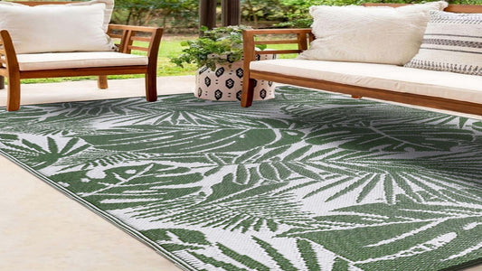 Tropical leaf patterned rug on a patio with wooden chairs and a couch.